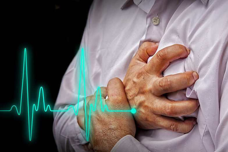 Mann hält sich vor Schmerzen im Herzbereich die Brust. Zusätzliche Abbildung eines EKG-Verlaufes.