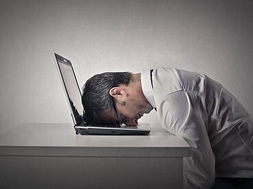 Chronisches Erschöpfungssyndrom: Mann liegt mit Kopf auf Laptop-Tastatur